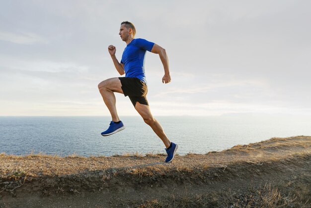 사진 성숙 한 남자 운동 선수 는 하늘 과 바다 를 배경 으로 한 산길 에서 달린다