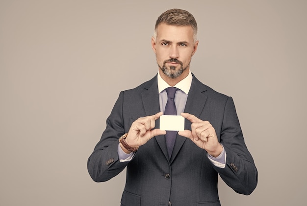 Mature man banker with grizzled hair in suit showing credit or debit card copy space manager