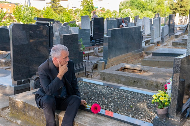 mature man in black clothes on cemetery holding a flower and mourning for family loss