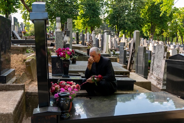 mature man in black clothes on cemetery holding a flower and mourning for family loss