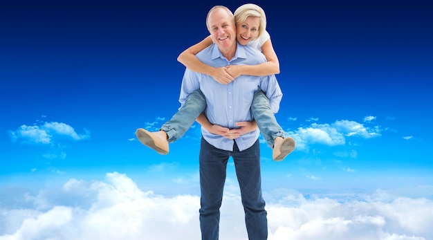 Mature man carrying his partner on his back against bright blue sky over clouds