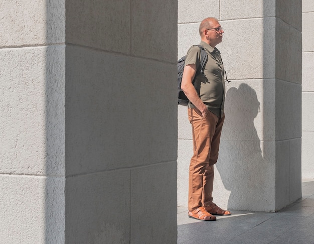 Mature man in casual clothes with backpack standing among building columns