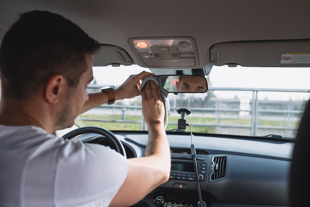 Зрелый мужчина чистит зеркало заднего вида в роскошном автомобиле с тканью. Селективный акцент на мужские руки.