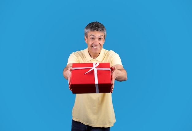 Mature man giving gift box congratulating you on blue background