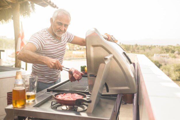 Mature man grilling steaks on a gas grill on his penthouse terrace