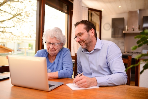 Фото Зрелый мужчина помогает пожилой пожилой женщине дома с документами и уроком компьютерного интернета