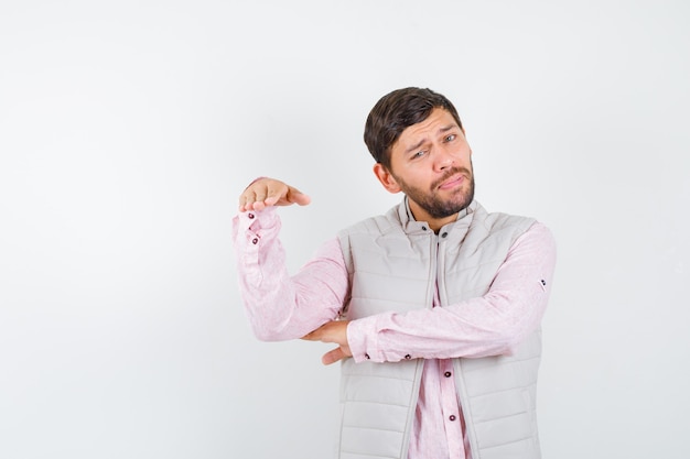 Mature man holding showing height gesture in shirt, sleeveless jacket and looking pensive. front view.