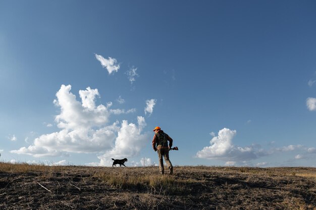 Mature man hunter with gun while walking on field with your dogs