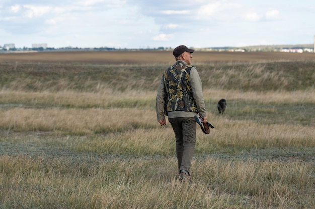 Mature man hunter with gun while walking on field with your dogs