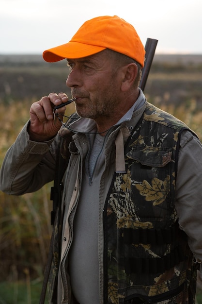 Mature man hunter with gun while walking on field