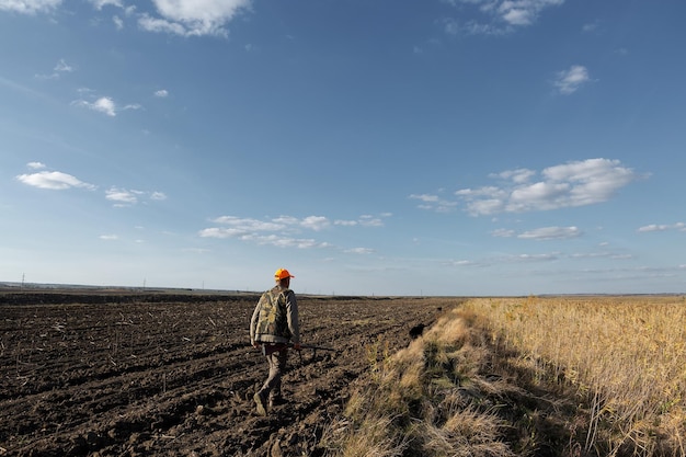 Mature man hunter with gun while walking on field