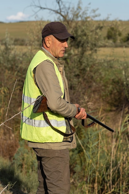 Mature man hunter with gun while walking on field