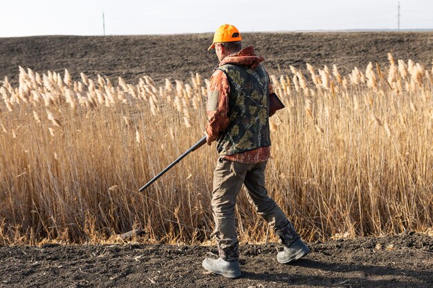 Mature man hunter with gun while walking on field