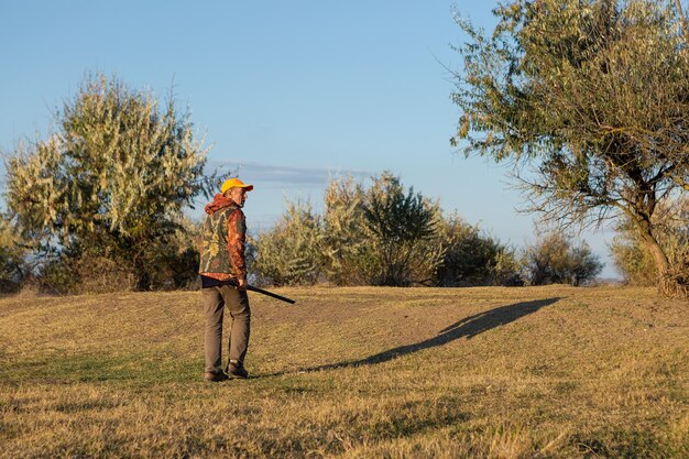 Mature man hunter with gun while walking on field