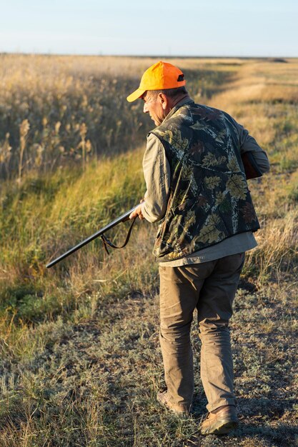 Photo mature man hunter with gun while walking on field