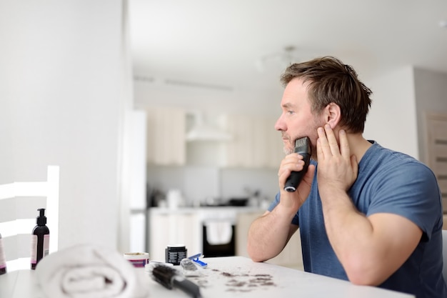 Mature man is shaving off his beard with electric razor at home