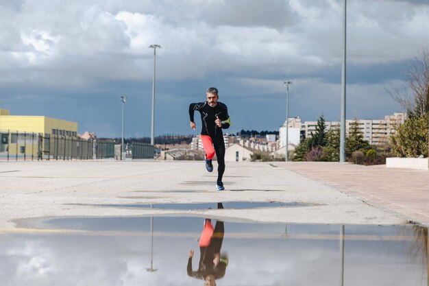 Foto uomo maturo che fa jogging sulla strada contro un cielo nuvoloso