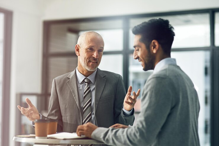 Photo mature man and male person for mentor paperwork and coffee in office for advice in business senior employee and intern as coworkers in meeting for brainstorming ideas and smile in corporate