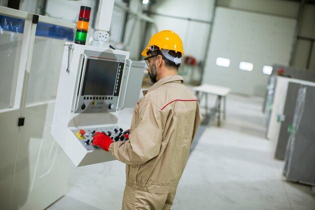 Mature man operating machine units in modern factory standing by control panel