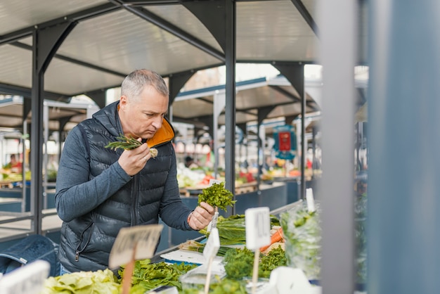 Mature man picking vegetables at farmers' market. 