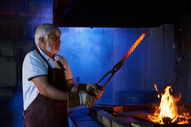 Photo mature man preparing metal over fire for forging