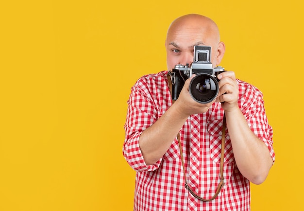 Mature man behind retro photo camera on yellow baqckground