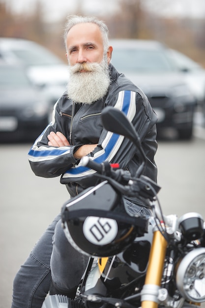 Mature man riding a motorcycle. Old male on motorbike. Bearded man outdoors driving.