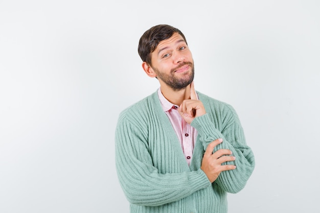 Uomo maturo in camicia, cardigan che tiene il dito sulla guancia e sembra felice, vista frontale.