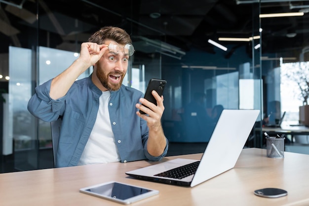Mature man shocked by bad news and online notification received on phone businessman at work