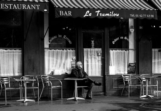 Зрелый мужчина сидит за столом в кафе на тротуаре.