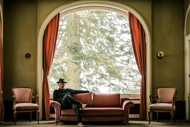 mature man sitting on sofa against window at home during winter