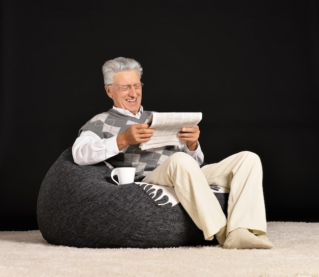 Mature man sitting with newspaper on a black background