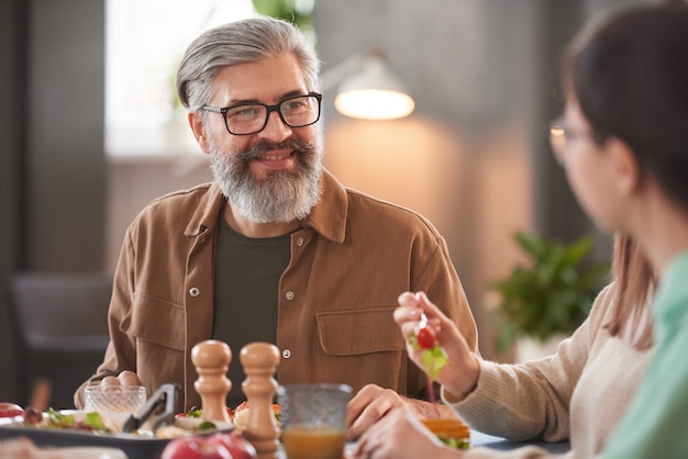 Mature man smiling and talking to the girl while having dinner at the table