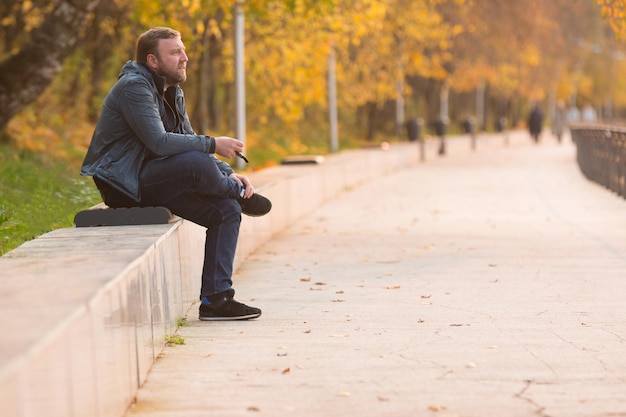 Photo mature man smoking while sitting on bench at park