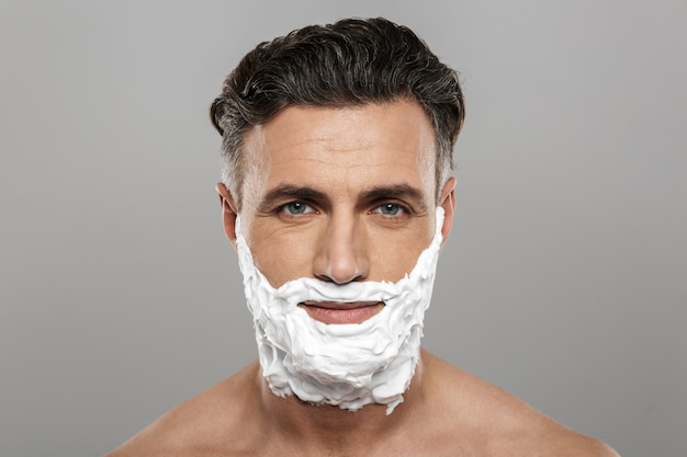 Mature man standing isolated with shaving cream on face.