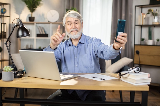 Mature man taking selfie with raised finger in home office