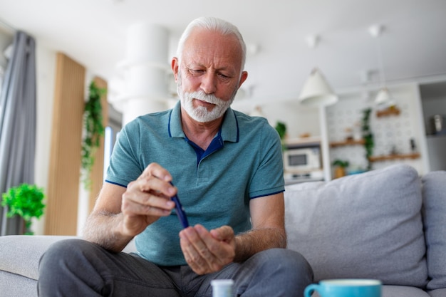 Mature man testing for high blood sugar Man holding device for measuring blood sugar doing blood sugar test Senioir man checking blood sugar level by glucometer and test stripe at home