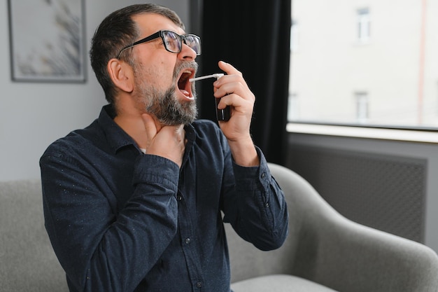 Mature man using an antiseptic throat spray at home