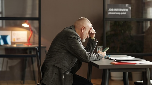 Mature man using his mobile phone at table while waiting for interviewer during job interview