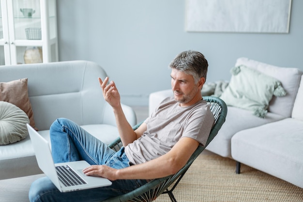 Mature man using a laptop while sitting in a home chair