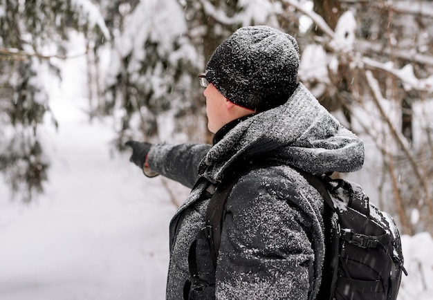 Mature man walking in snowy forest woods in snow on winter holiday pointing showing way with hand finger Person in cold weather nature outdoor