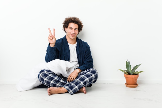指で番号2を示す家の床に座っているパジャマを着ている中年の男性。