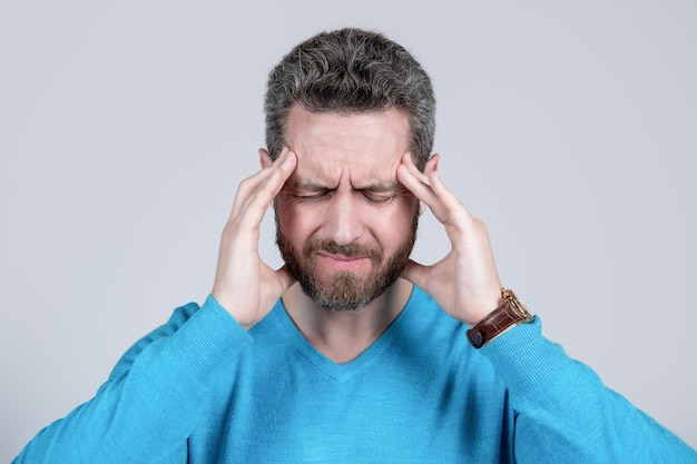 Mature man with beard suffer from headahce on grey background, health.