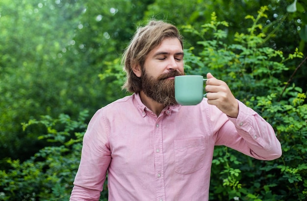 あごひげとトレンディな髪型の成熟した男は、朝、コーヒーを飲みます。