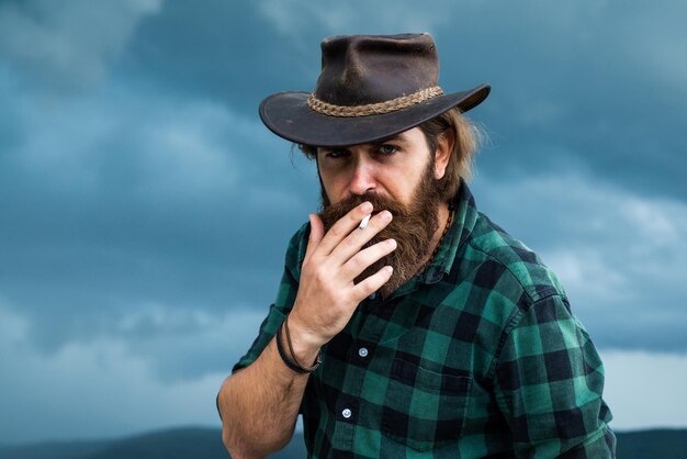 mature man with beard wear cowboy hat and smoking cigarette, west.