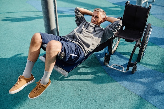 Mature man with disability lying on the sport equipment and training his press during sports trainin...