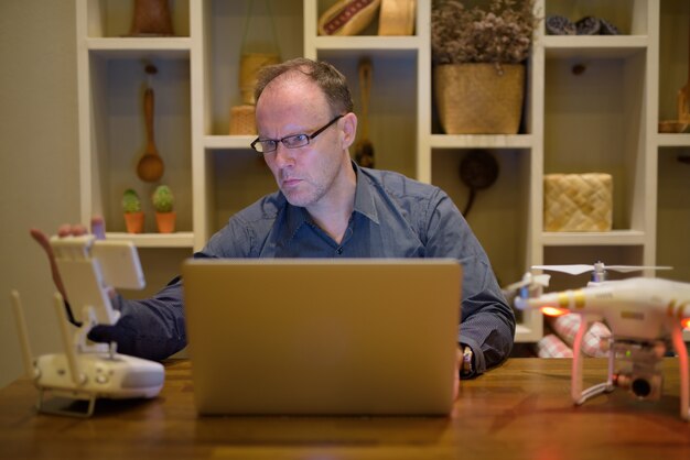 Mature man with drone and laptop in the dining room at home