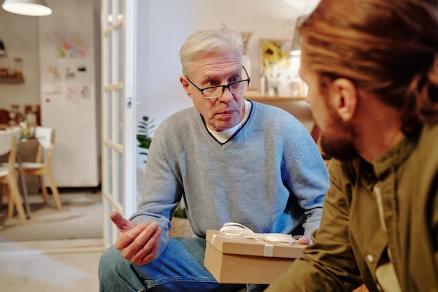 Mature man with giftbox talking to his son while sitting in front of him