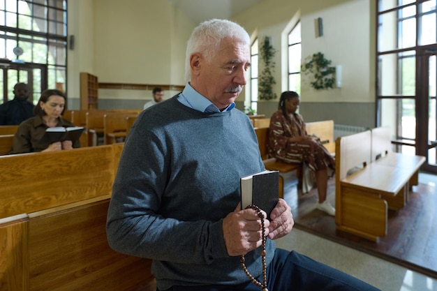 Mature man with holy bible and rosary beads in hands saying prayers