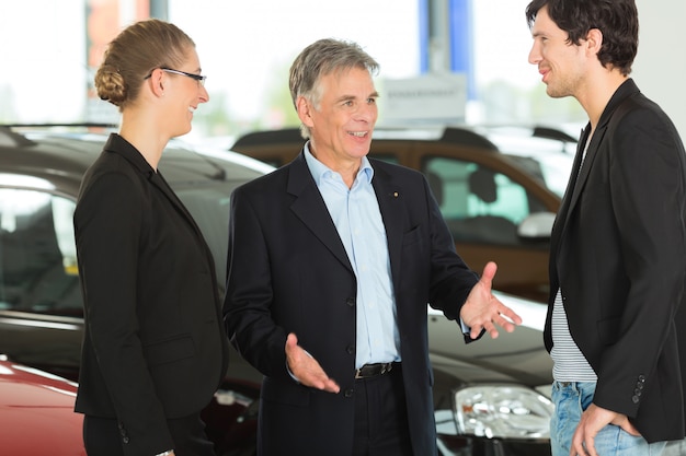 Photo mature man with young couple and autos in car dealership